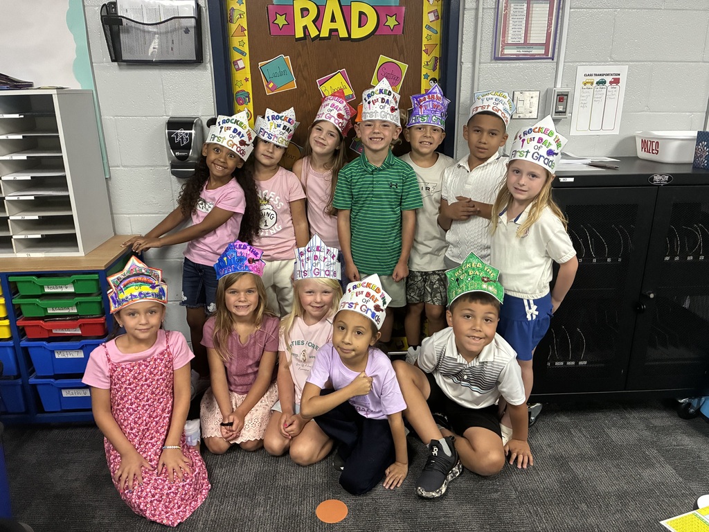 Several children, adorned with crowns, are gathered in a classroom, posing for a group photo.