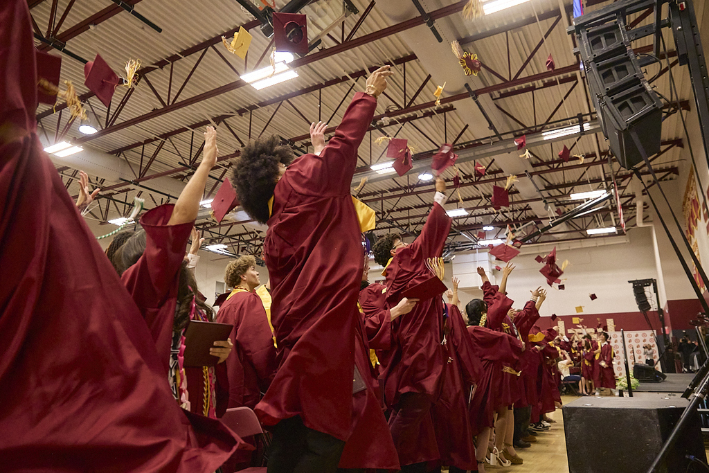 Graduates in cardinal and gold throwing caps at graduation ceremony