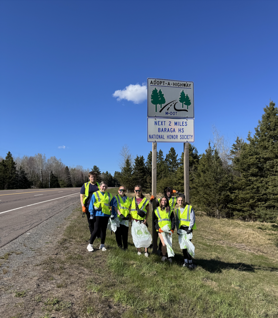 Baraga High School National Honor Society students standing in front of an Adopt a Highway sign.