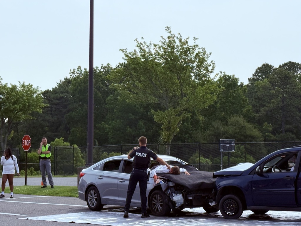 Picture of a police officer checking for a pulse on the student through the windshield. 