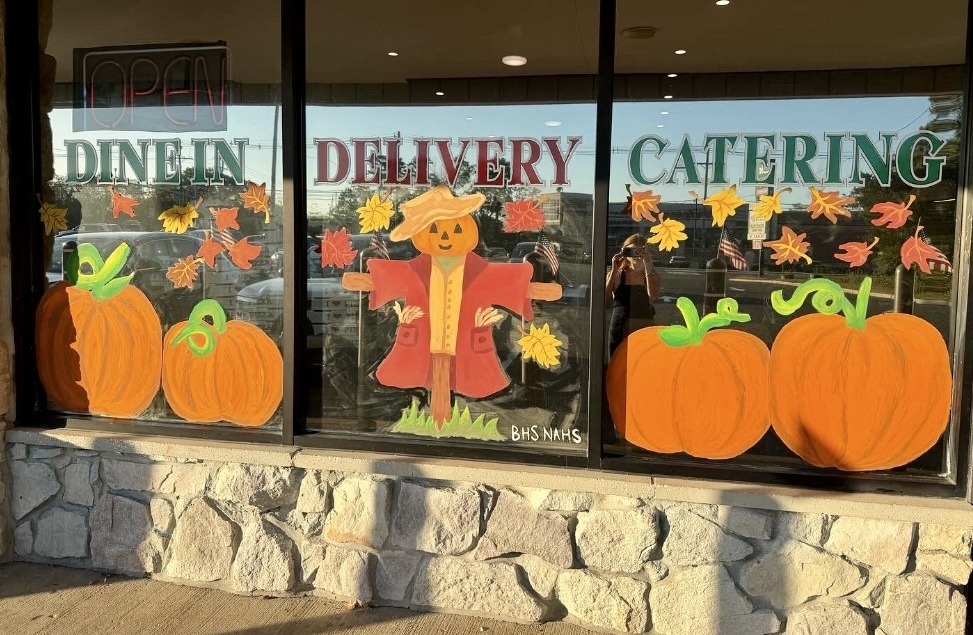 Image of pumpkins and a scarecrow surrounded by fall leaves.