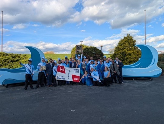 Image of all the students and staff posing with the banner and the awards that were received. 