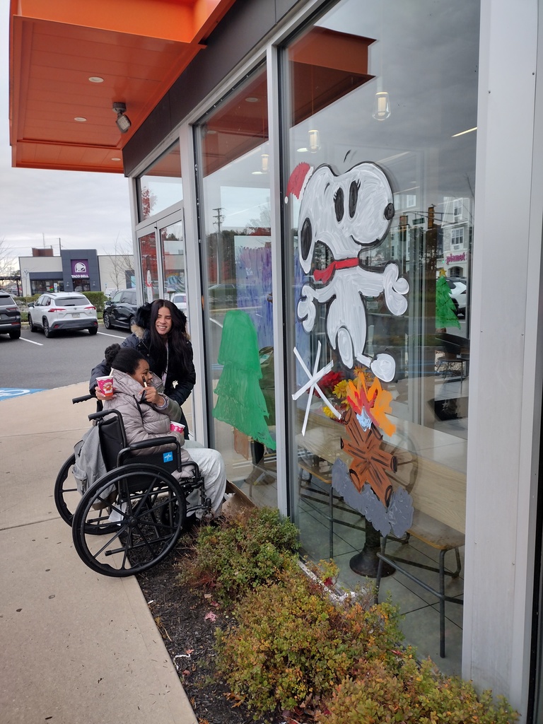 Image of a student in a wheelchair with a staff member painting a Christmas tree. 