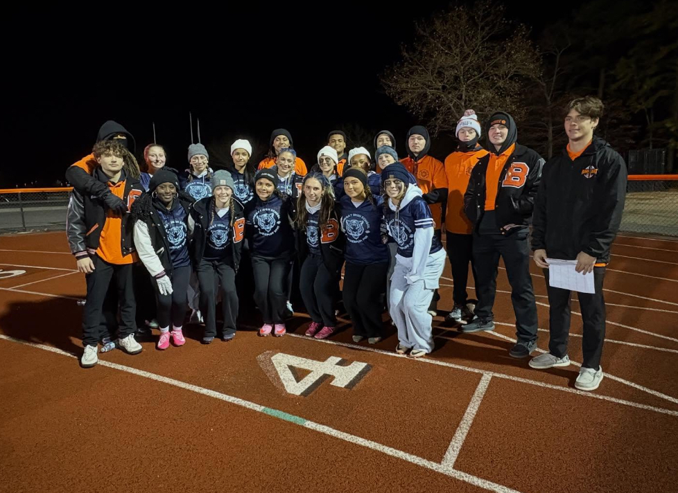 Image of the junior girls team posing with the student coaches on the track. 