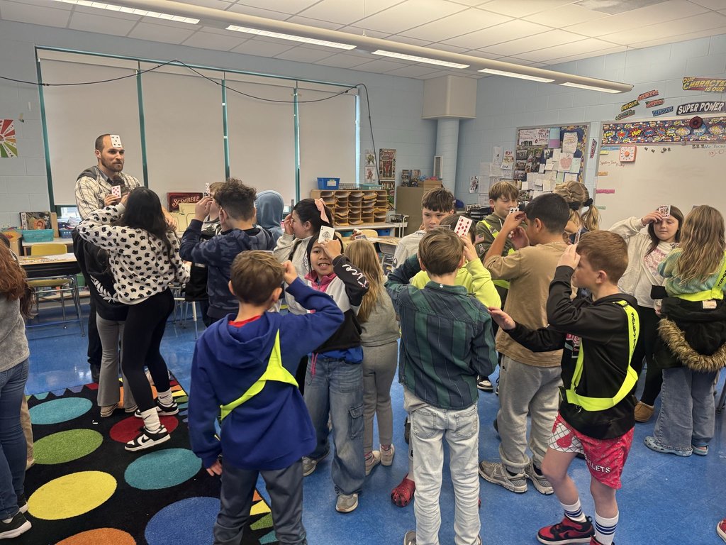 Image of a 4th-grade class participating in an activity holding playing cards up to their foreheads. 