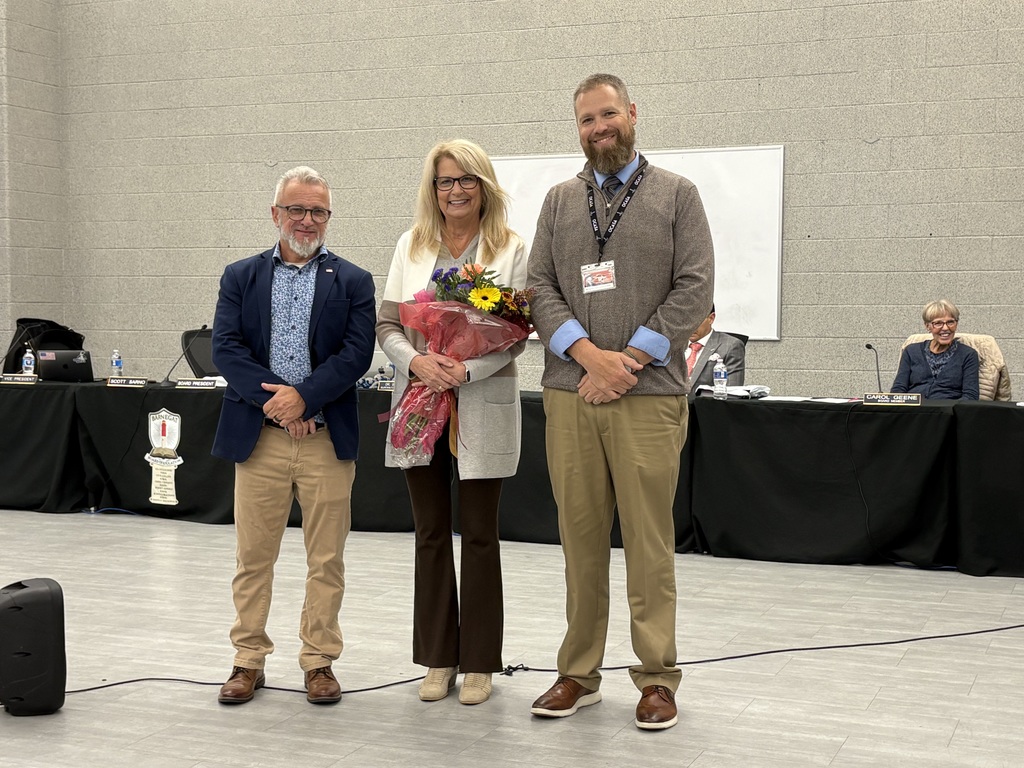 Image of Doreen holding flowers posing with the Superintendent and Board President. 