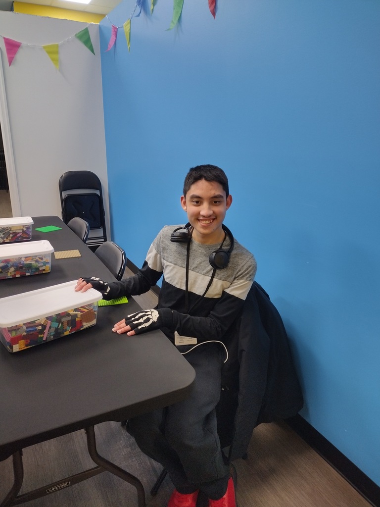 Image of a student sitting at a table with a container of legos.  