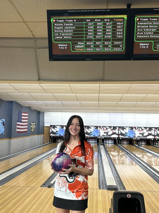 Image of Jamie holding her bowling ball posing below the scoreboard. 