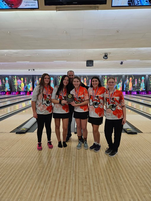 Image of the girls bowling team and their coach posing wearing medals and holding a plaque. 