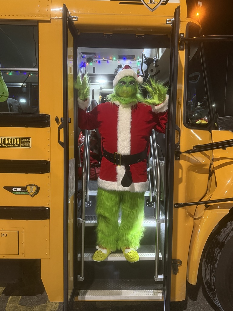 Image of the male bus driver standing inside the doors of the bus dressed up as the Grinch.