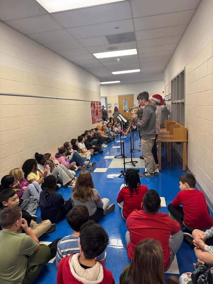 Image of members of the BHS band playing music in the hallway of the Donahue School while students sit in the hallway to listen. 