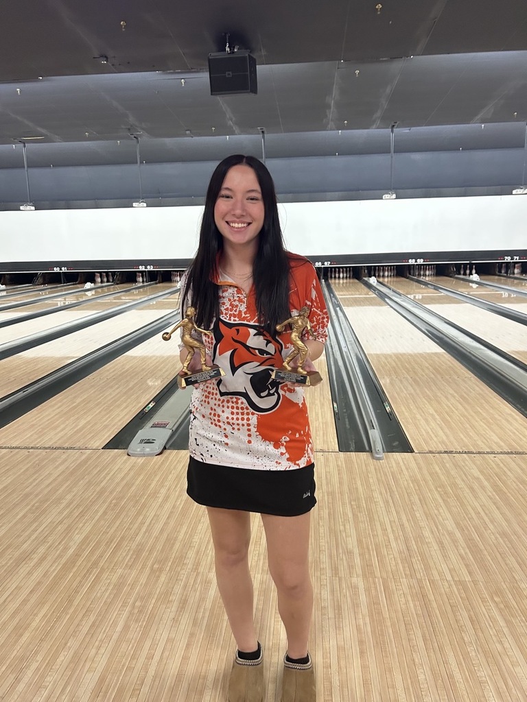 Image of Jamie holding her two trophies standing in front of the bowling lane. 