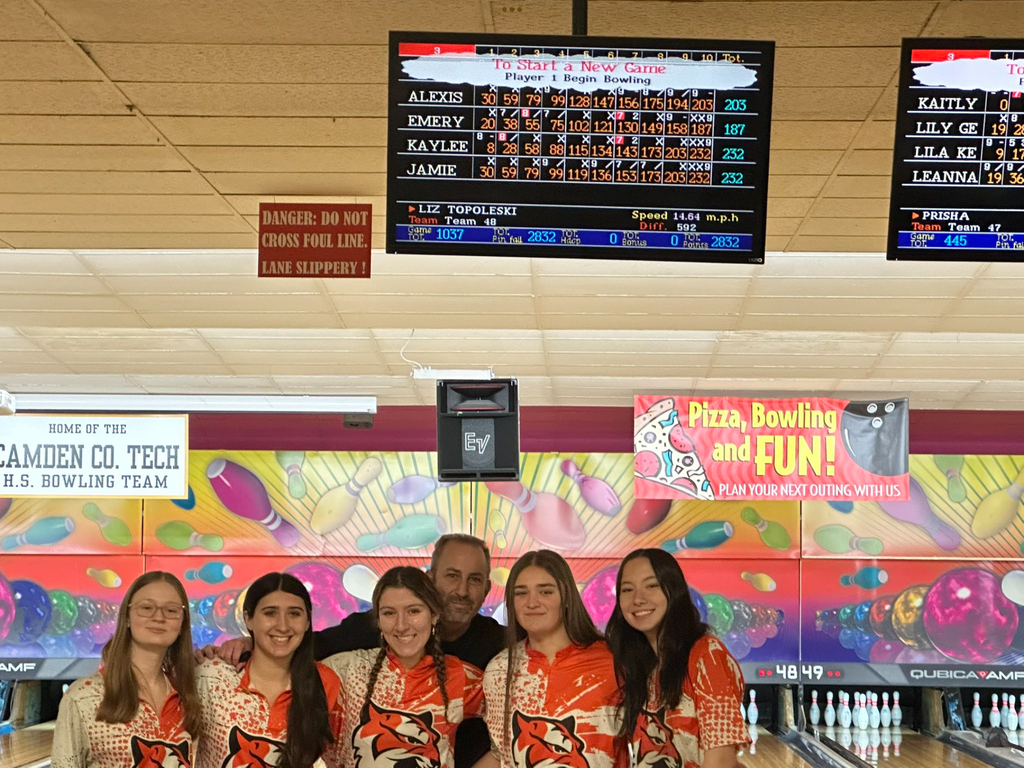 Image of the girls bowling team and their coach posing underneath the scoreboard. 