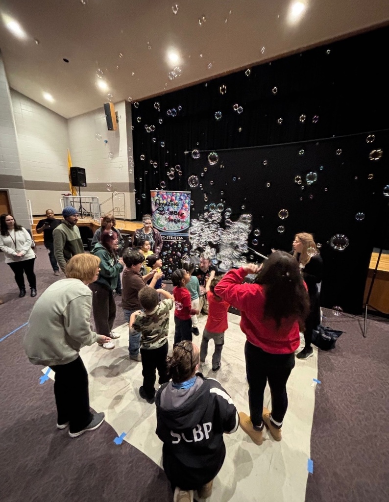 Image of a class standing on a mat with bubbles in the air over their heads. 