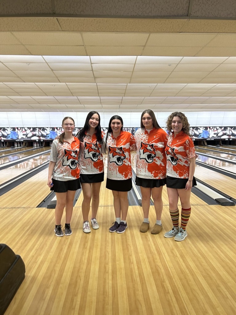 Image of the girls bowling team posing in front of their bowling lane. 