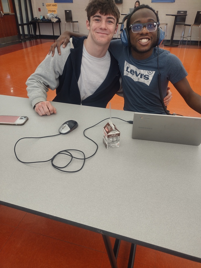 Image of two boys sitting at a table with a computer and posing with their arms around one another.
