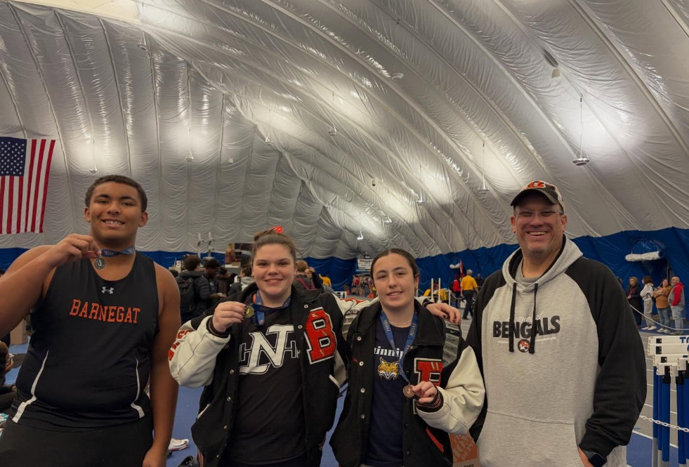 Image of Zechariah, Ellie, and Riley posing with the throws coach holding out the medals that are around their necks.