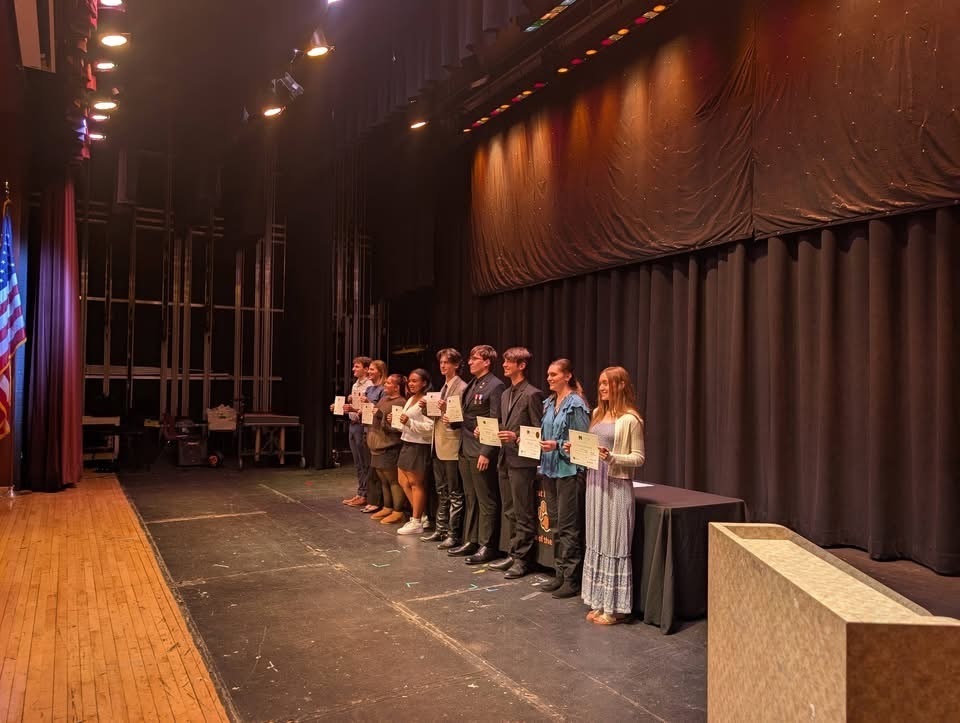 Image of nine students posing on stage holding their certificates.  