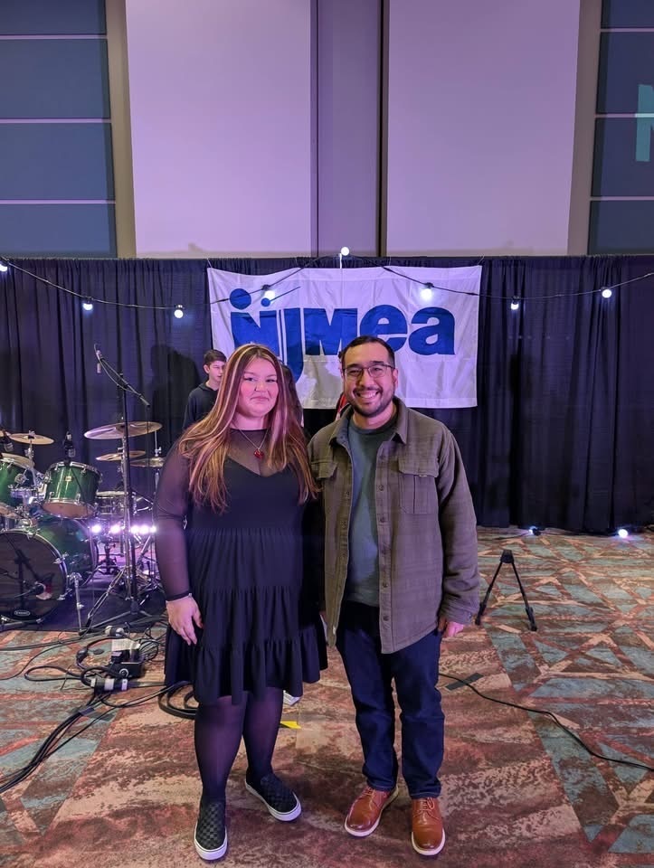 Image of Paige Mairowicz posing with  sponsor Mr. Wes Brown in front of a percussion set and NJMEA banner at the NJMEA Conference. 