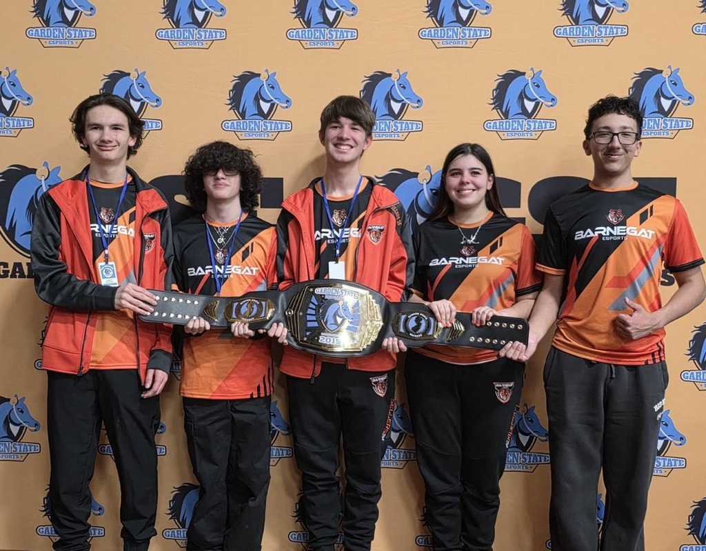 Image of the five Overwatch Esport team members holding the championship belt in front of the Garden States Esports banner wall. 