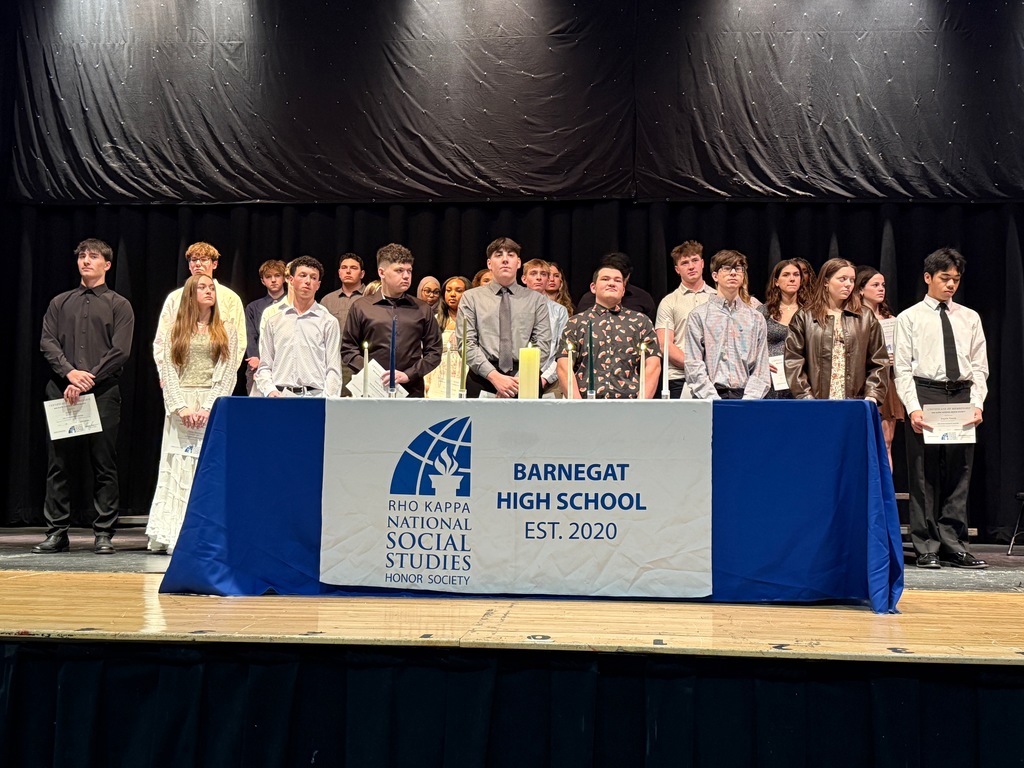 Image of all of the Rho Kappa inductees standing on the stage in front of table with their banner and candles. 