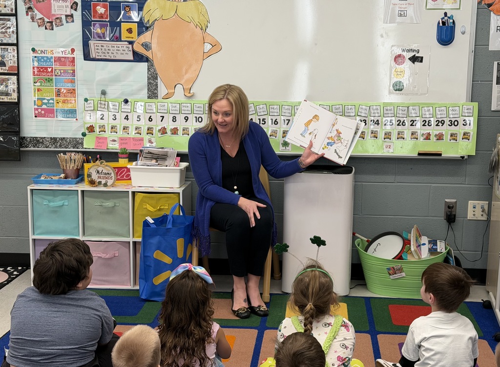 Image of the Principal sitting in a chair reading to a class sitting on a rug. 