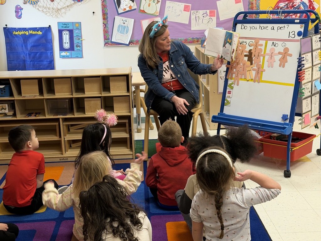 Image of a staff member sitting in a chair reading to a class sitting on a rug. 