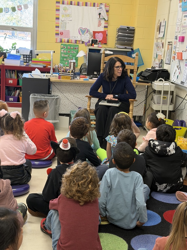 Image of the curriculum supervisor sitting in a chair with a book on her lap getting ready to read to a class.  
