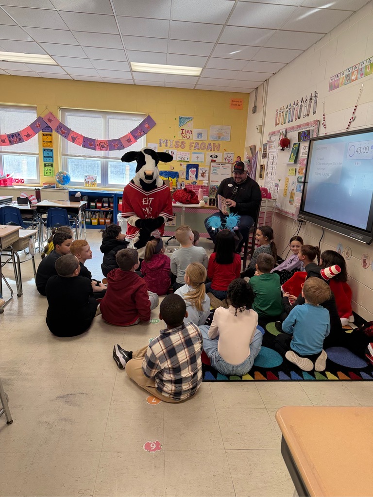 Image of the owner of Chick-Fil-A and the mascot Milkshake sitting on chairs getting ready to read to a class. 
