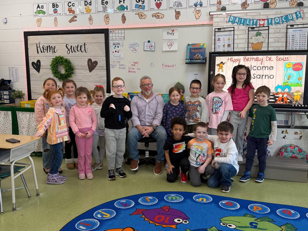 Image of the Board of Education president sitting in a chair surrounded by the students who he read to. 