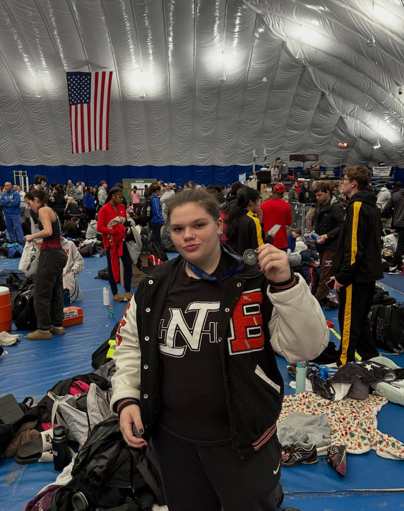 Image of Ellie posing in her varisty jacket holding her medal up that is hanging around her neck. 