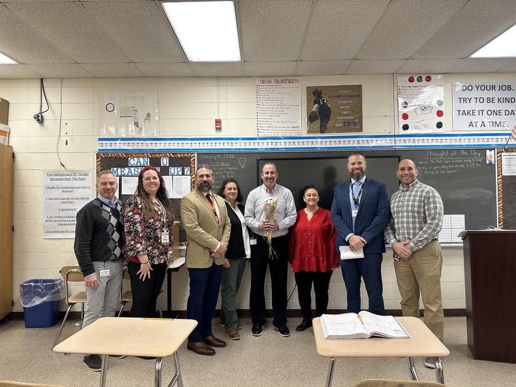 Image of Mr. Gordon holding a bouquet of flowers posing with district and building administrators. 