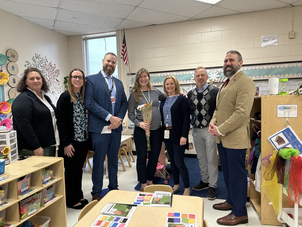 Image of Mrs. Carroll holding a bouquet of flowers posing with district and building administrators. 