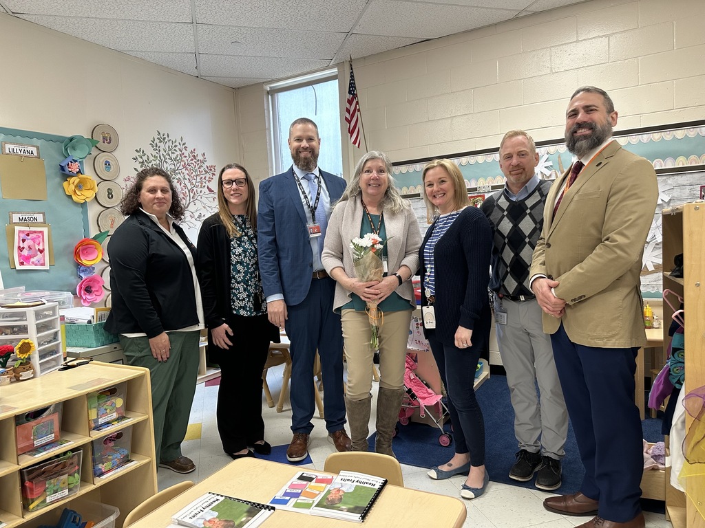 Image of Mrs. Hathaway holding a bouquet of flowers posing with district and building administrators. 
