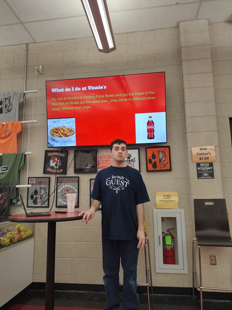Image of a male student posing in front of his powerpoint about his job at Vinnie's. 