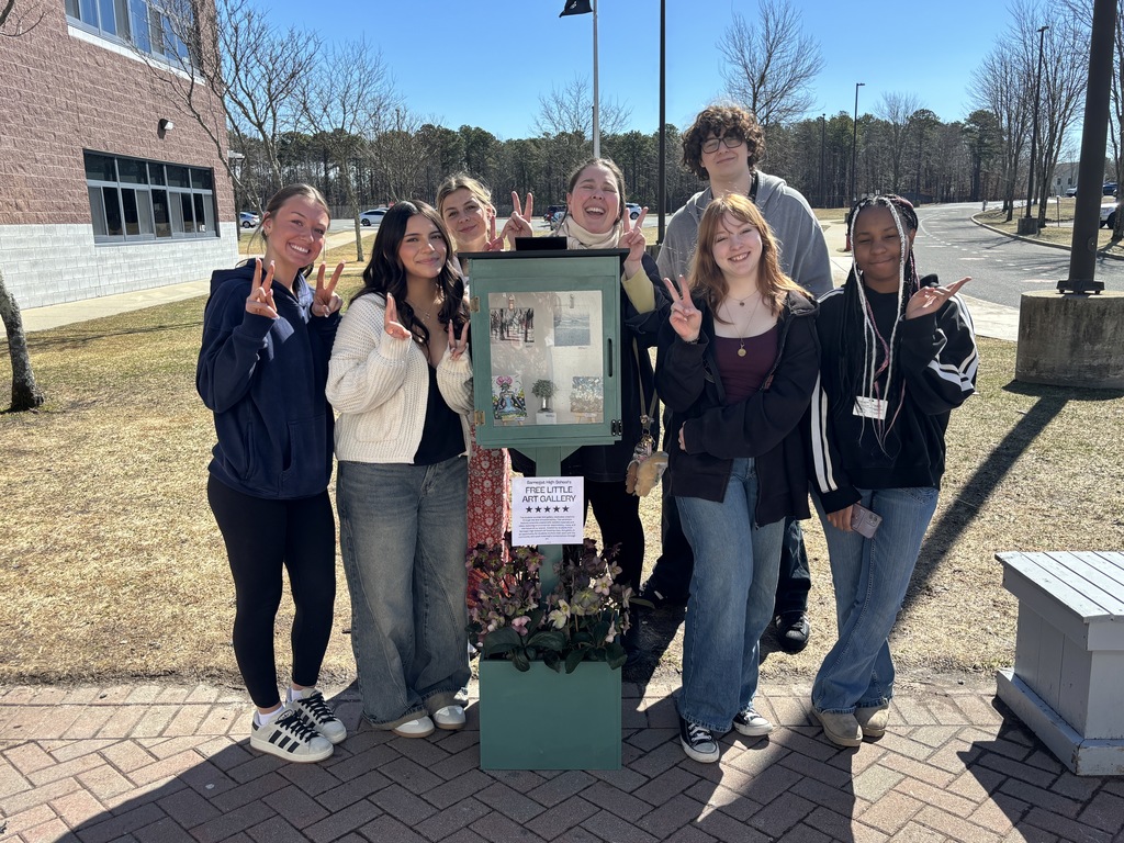 Image of the AP drawing clas with Ms. Polcino posing in front of their mini art gallery. 