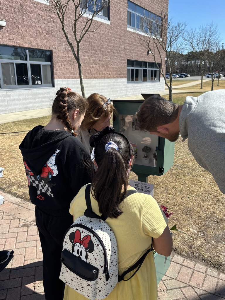 Image of two adults and two students checking out the mini art gallery projects on display. 