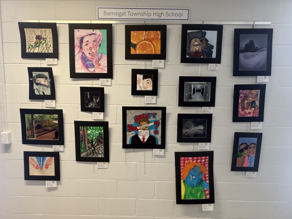 Image of the drawings and paintings on display on  a wall under a Barnegat High School banner and information cards attached to each piece.