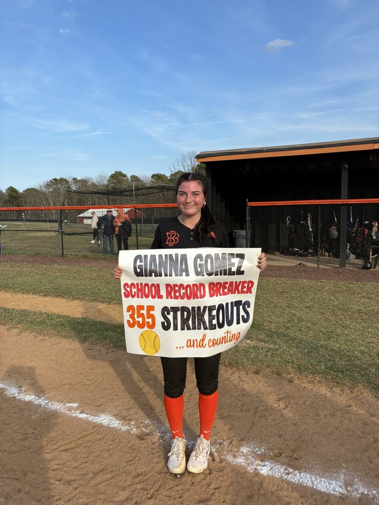 Image of Gianna posing on the field with holding a sign that says her her name, school record breaker, 355 strikeouts and counting with a softball. 