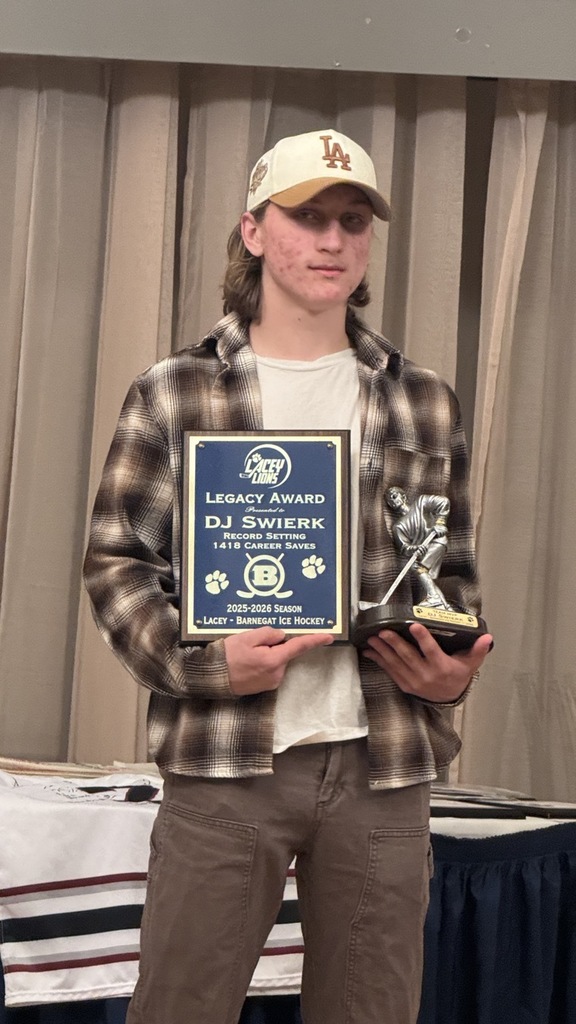 Image of DJ at an awards banquet posing with a plaque for career saves and a ice hockey player plaque. 