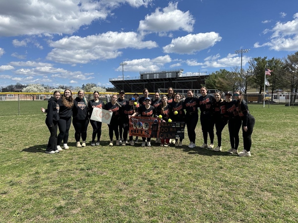 Image of the girls softball team hold signs in support of Riley's 100th hit. 