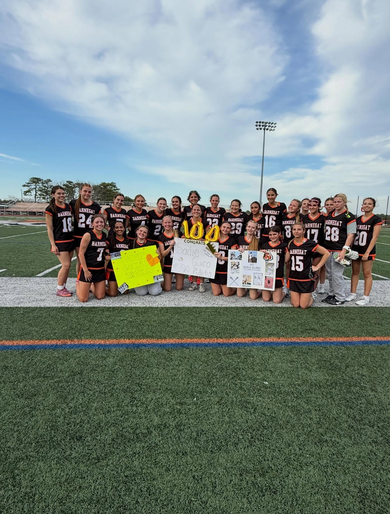 Image of the girls lacrosse team holding signs and balloons in support of Sadie's 100th point. 