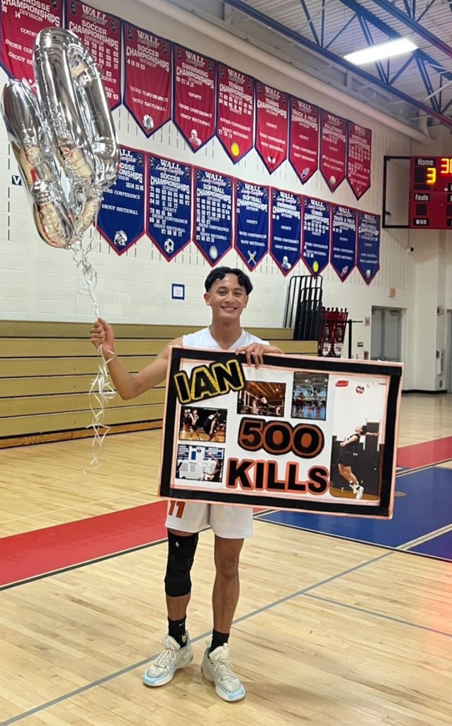 Image of Ian holding balloons and a sign that says his name. has pictures of him playing on the courts, and states 500 kills. 