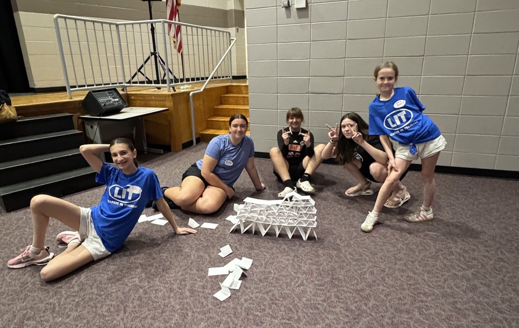 Image of five LIT's posing with their index card tower that they were building on the floor.  