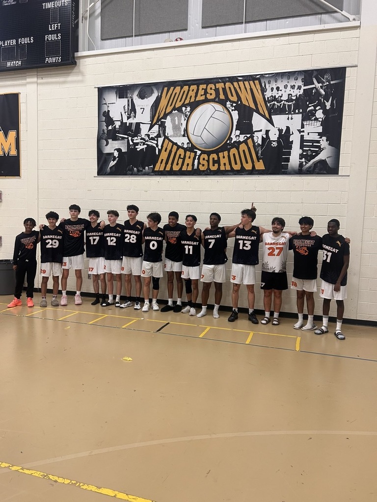 Image of the boys volleyball team posing together under the Moorestown High School Volleyball banner. 