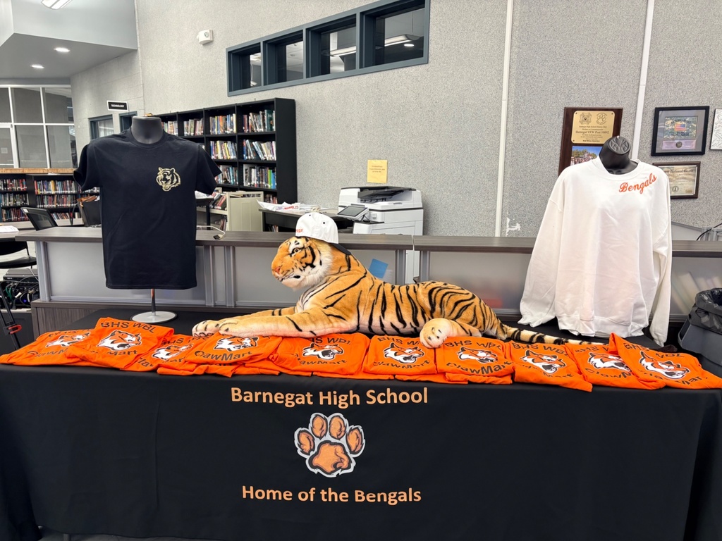 Image of a display table with a Barnegat High School tablecloth, a stuffed Bengal tiger wearing a hat, a tshirt display, a sweatshirt display, and  Clawmart t-shirts for each guest. 
