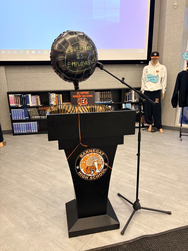 A podium with the BHS logo and black balloon that says Everyone is Employable with a clothing display in the background. 