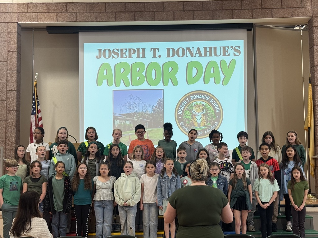 Image of the JTDS select chorus singing an Arbor Day song on risers in front of the stage as Mrs. Kuntz directs the students. 