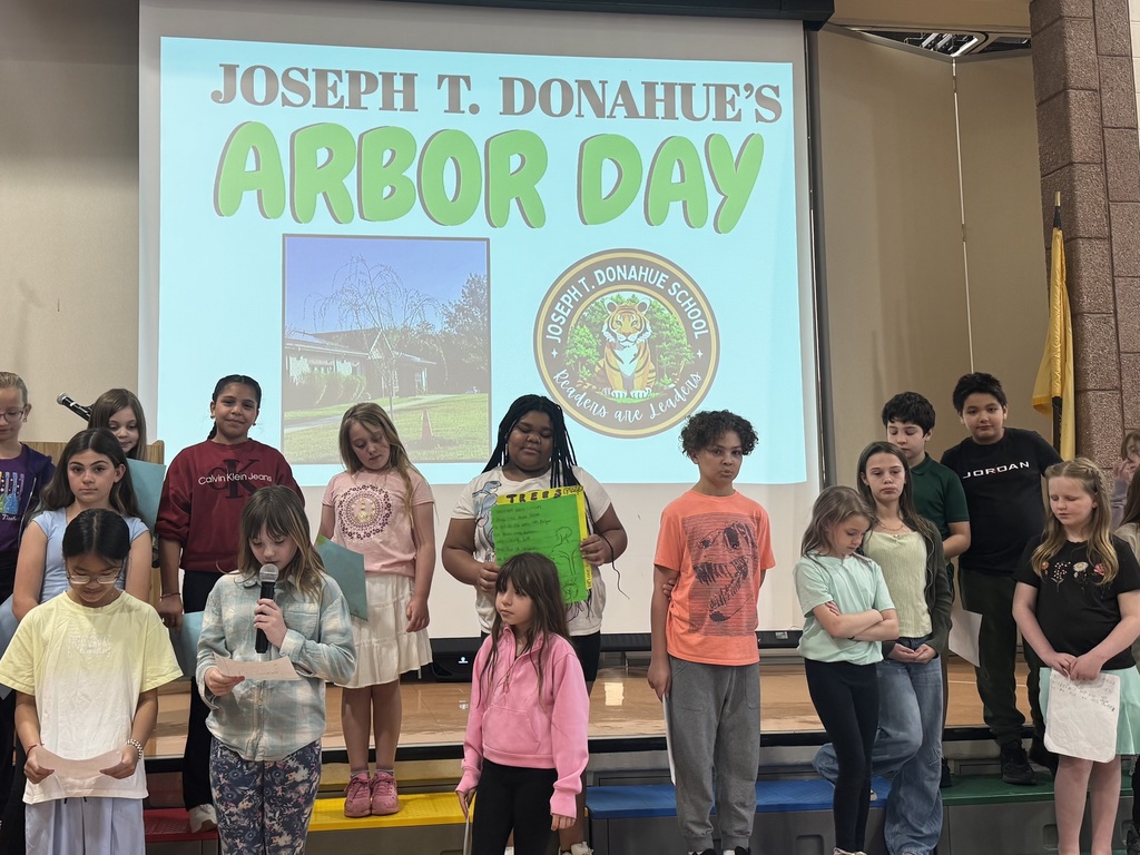 Image of the JTDS students standing on risers in front of the stage reading poems and stories that they wrote for Arbor Day. 