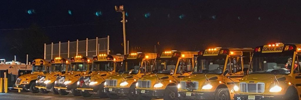Image of the Barnegat school buses lined up in a row at night with their lights on. 
